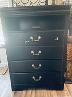 Front view of black chest showing four drawers, open shelf, hardware, scuffs