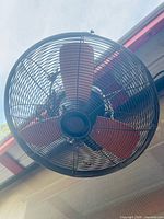Close view of front of black wire-caged fan with three red-brown blades