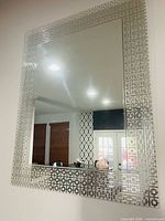 Full view of rectangular wall mirror mounted on wall showing beveled center and silver geometric frame