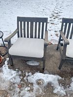 Front view of one armchair showing slatted back, arms, and beige cushion