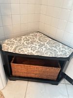 Corner bench positioned in tiled corner with cushion on top and basket inside