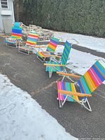 Four rainbow striped and one blue-green striped folding chairs lined up outdoors