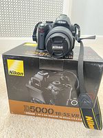 Camera body with lens and strap on top of Nikon retail box