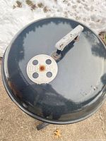 Lid top showing black porcelain finish and Weber vent with rust