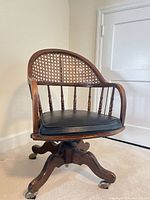full view of wooden swivel chair showing cane back, seat, base, casters