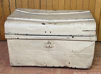 closed cream metal toy chest front view, shows dents and latch