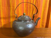Front view of antique copper kettle showing overall form and brass handle