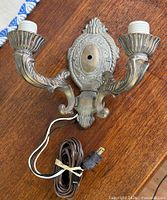Front view of brass double arm wall sconce with cord visible