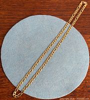 Full view of gold-washed sterling silver Figaro chain laid straight on blue circle background