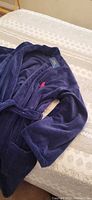 Full view of navy bathrobe laid on bed showing belt and pockets