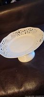 Full view of white porcelain footed cake stand on leather surface