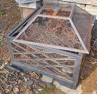 Steel square fire pit with mesh hood, fireplace tongs and stand visible