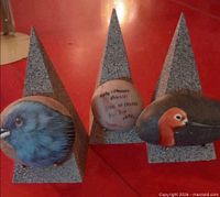 Three painted river rocks on triangular stone stands, front views