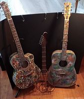Two custom painted acoustic guitars on floor stands with wire guitar sculpture between