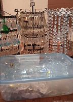 Multiple racks holding assorted clear and iridescent glass prisms and strands beside plastic bin