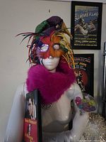 mannequin with mask, jester hat, pink fur collar, poster art in background, Elvis DVD visible