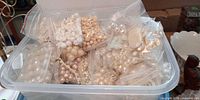 Large clear tub filled with multiple sealed bags of white and pearl beads