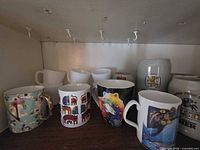 Front row of printed ceramic mugs and two steins on shelf