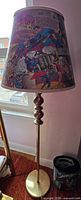 Full view of metal floor lamp with comic-print shade beside wastebasket