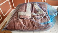 Folded queen duvet with two matching pillow shams in blue plastic storage bag on table
