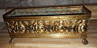 Front view of hammered brass planter tray showing floral relief, claw feet, and interior patina