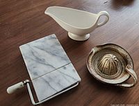 All three items on wooden surface: marble cheese cutter, ceramic gravy boat, earthenware juicer