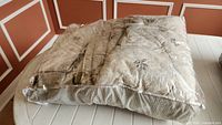 Folded beige floral bedding set in plastic wrap on table