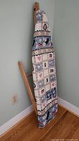 Full view of wooden folding ironing board leaning against wall with patterned cotton cover