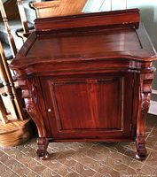 Front view of closed desk highlighting mahogany finish, carved supports, cabinet door, ball-and-claw feet