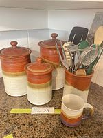 Group shot of three stoneware canisters, utensil crock with utensils, and coffee mug