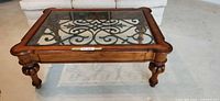 Full view of coffee table showing wood frame, glass top, wrought iron design, spindle legs