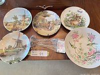 All four decorative plates, floral bowl, and package of wire hangers laid out on table