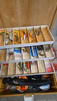 Interior of tackle box showing multiple trays of assorted fishing lures and spoons