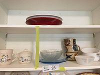 Shelf view with red platter, stoneware cream and sugar, speckled mugs, glass bowls and white bowls