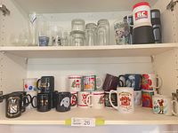 Open cupboard showing mugs on lower shelf and glasses on upper shelf