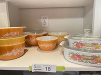 Overall lot on shelf showing Pyrex casseroles, mixing bowls, CorningWare bakers with lids