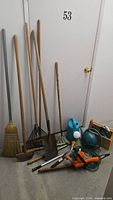 Group shot of all yard tools leaning against wall, watering cans and trimmer visible