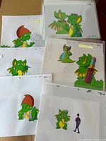 Group of cels in sleeves showing multiple dragon characters with hats, wings, and props.