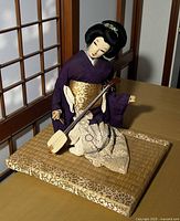 Full view of geisha ningyo doll in purple kimono holding shamisen, seated on brocade-edged tatami mat