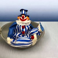 Blue-striped Korky clown doll seated inside original plastic bubble display case