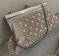 Front view of cream clutch with silver beads, sequins, chain, metal frame