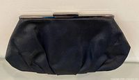 Front view of black satin clutch showing gathered fabric and frame