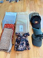 Overview of folded fabrics, doll dress and three stacked baseball caps on wooden floor