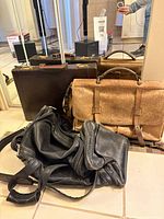 All three leather bags grouped: dark brown briefcase, tan satchel, black duffel