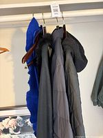 Four outerwear pieces hanging: blue scarf, black faux-fur trimmed shawl, grey puffer, black quilted jacket
