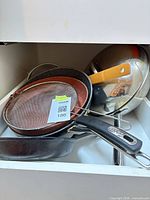 Drawer view showing stacked frying pans, wok, strainers
