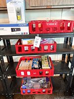 Overall lot on shelving: Garmin GPS, Alpine stereo, four red Coca-Cola crates holding boxed bulbs and showerhead kit