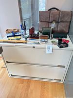Overall shot showing filing cabinet, briefcase, and assorted office supplies on top