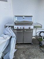 Front view of Weber Genesis 4-burner natural gas grill showing lid, control panel, cabinet and partially removed cover