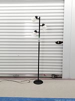 Full view of black metal floor lamp with three white shades